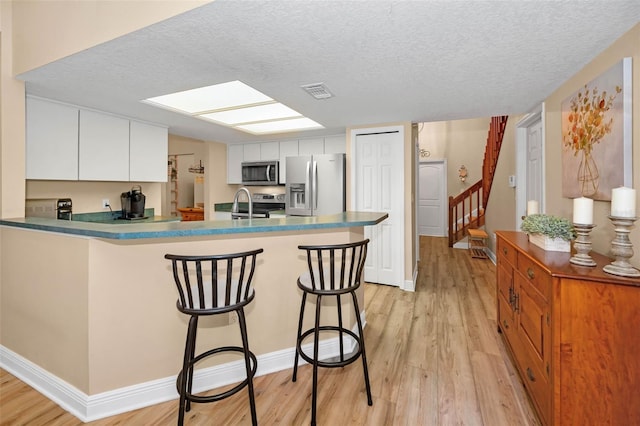 kitchen with light wood-style flooring, a kitchen breakfast bar, appliances with stainless steel finishes, a peninsula, and white cabinets