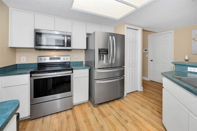 kitchen with a sink, stainless steel appliances, white cabinets, dark countertops, and light wood-type flooring