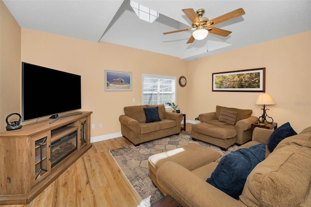 living area with baseboards, light wood-style floors, ceiling fan, and vaulted ceiling