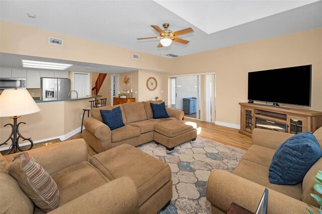 living area with light wood finished floors, visible vents, a ceiling fan, and baseboards