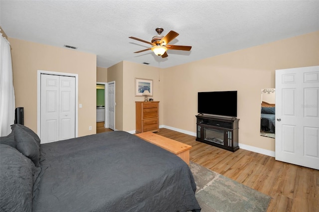 bedroom featuring a ceiling fan, baseboards, visible vents, light wood finished floors, and a textured ceiling