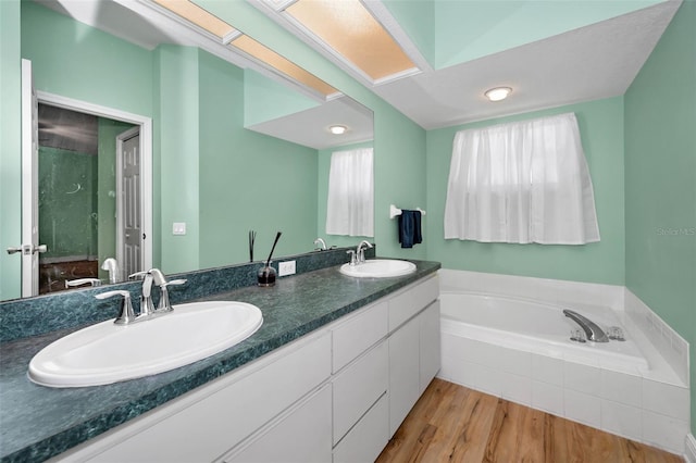 full bathroom with double vanity, a bath, wood finished floors, and a sink