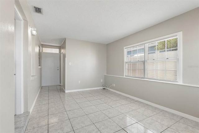 empty room featuring a textured ceiling, light tile patterned flooring, visible vents, and baseboards