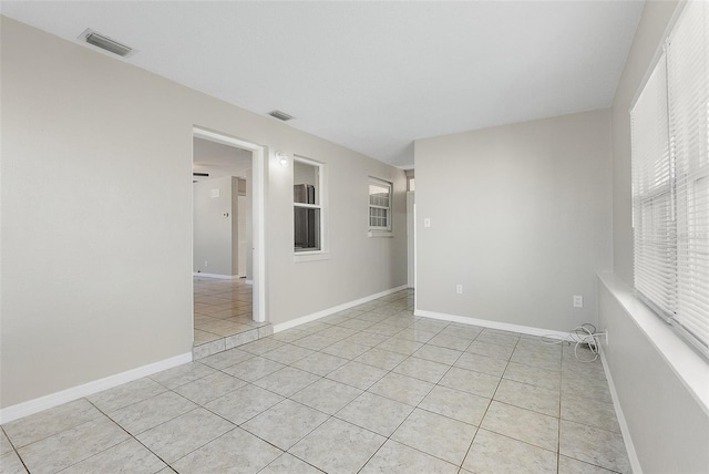 empty room with light tile patterned floors, a healthy amount of sunlight, visible vents, and baseboards