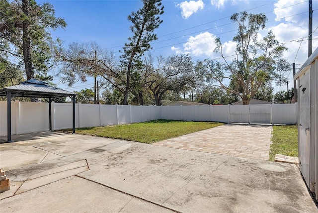 view of patio / terrace featuring a gazebo, concrete driveway, a fenced backyard, and a gate