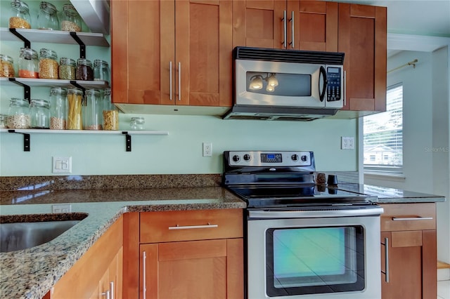 kitchen featuring open shelves, stainless steel appliances, brown cabinetry, and dark stone countertops