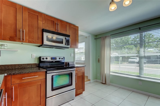 kitchen with light tile patterned floors, stainless steel appliances, baseboards, and brown cabinetry