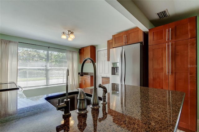 kitchen with brown cabinetry, visible vents, dark stone countertops, and stainless steel fridge with ice dispenser