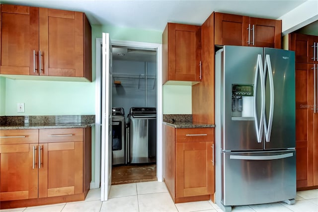 kitchen featuring washer and clothes dryer, dark stone counters, brown cabinetry, stainless steel fridge with ice dispenser, and light tile patterned floors