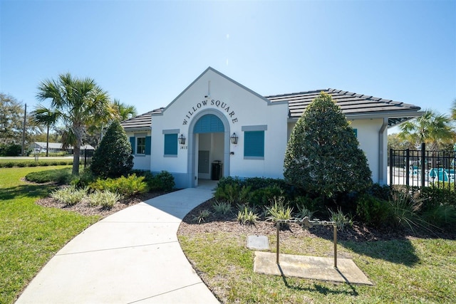 view of front of house with a tiled roof, fence, a front lawn, and stucco siding