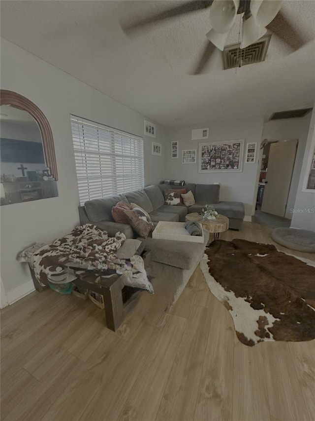 living room featuring a textured ceiling, ceiling fan, wood finished floors, visible vents, and baseboards