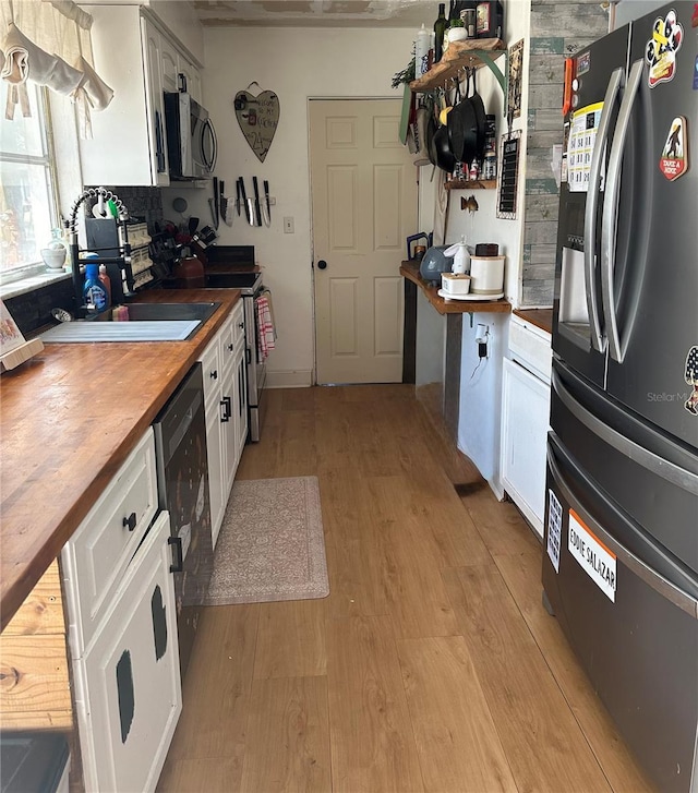 kitchen featuring appliances with stainless steel finishes, butcher block counters, white cabinets, and light wood-style flooring