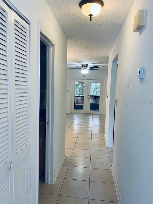 corridor with french doors, a textured ceiling, baseboards, and light tile patterned floors