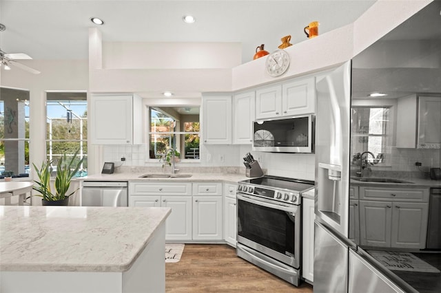 kitchen with light wood finished floors, appliances with stainless steel finishes, backsplash, and a sink