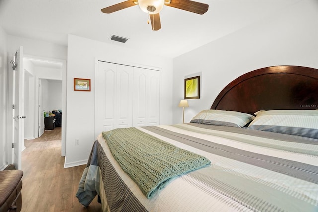 bedroom with wood finished floors, visible vents, baseboards, a ceiling fan, and a closet