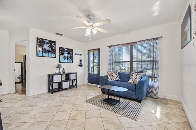 living area with light tile patterned floors, ceiling fan, visible vents, and baseboards