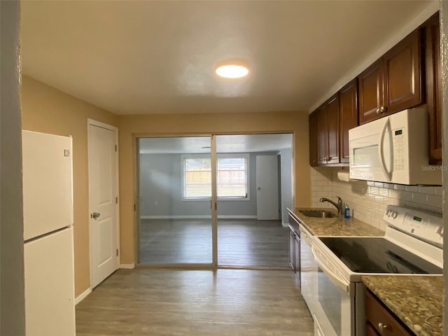 kitchen featuring white appliances, a sink, light wood-style floors, dark brown cabinets, and decorative backsplash