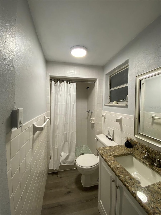 full bath featuring toilet, wood finished floors, vanity, tile walls, and tiled shower