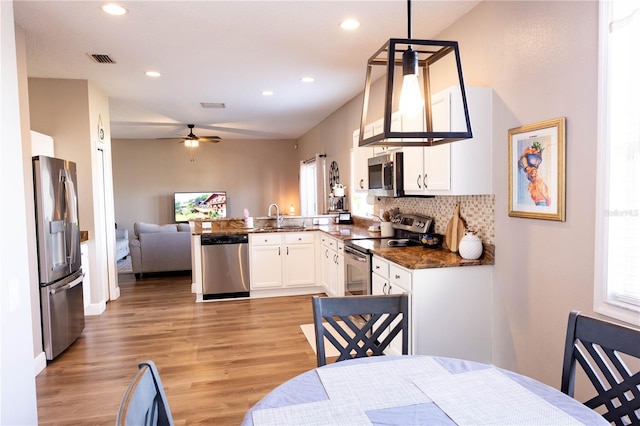 kitchen with appliances with stainless steel finishes, open floor plan, white cabinets, a sink, and a peninsula