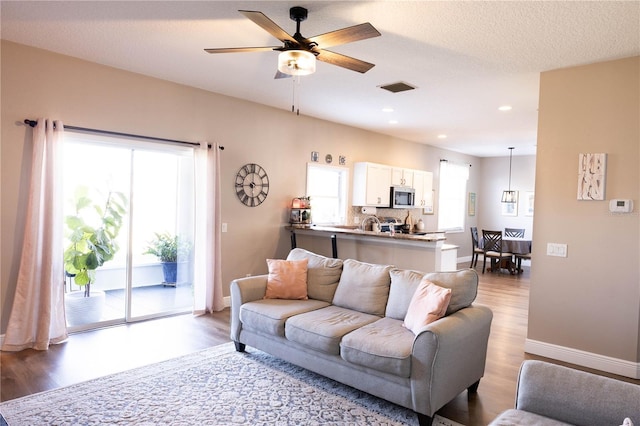 living room featuring ceiling fan, a textured ceiling, wood finished floors, visible vents, and baseboards