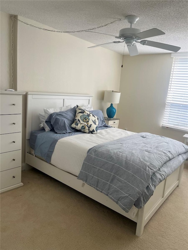 bedroom featuring light colored carpet, ceiling fan, and a textured ceiling