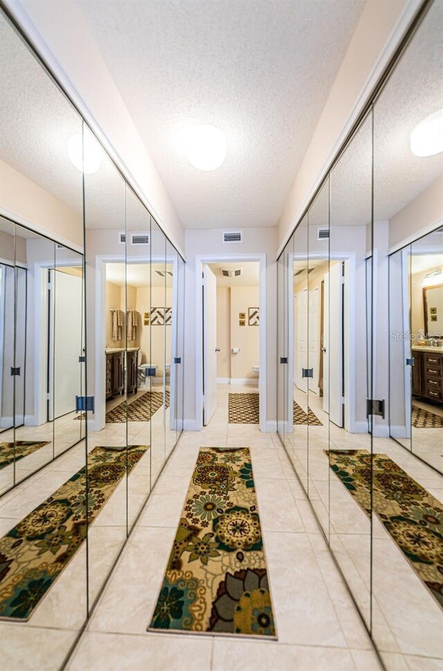 hallway featuring visible vents, a textured ceiling, baseboards, and tile patterned floors