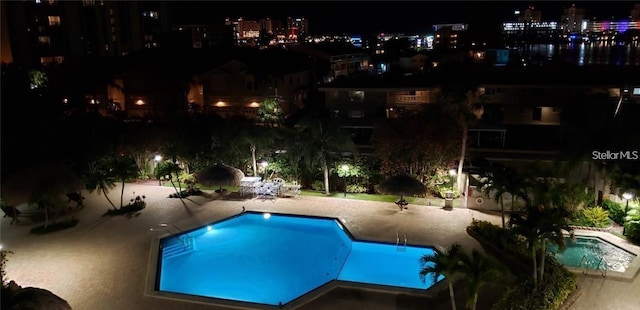 pool at twilight with a view of city lights, a patio area, and an outdoor pool