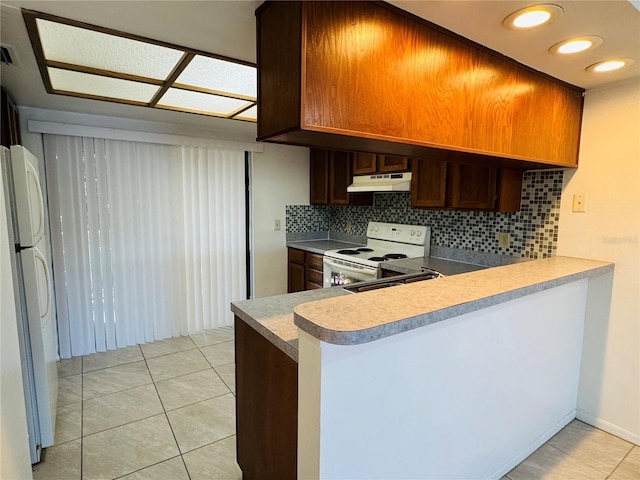 kitchen with under cabinet range hood, light tile patterned floors, decorative backsplash, a peninsula, and white appliances