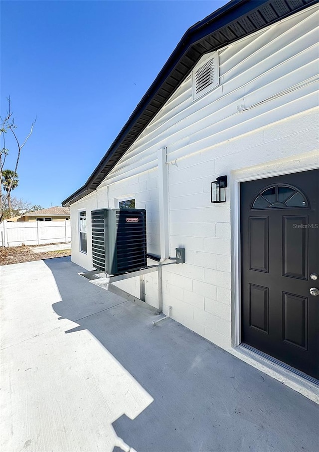 view of side of home featuring concrete block siding, fence, and central air condition unit