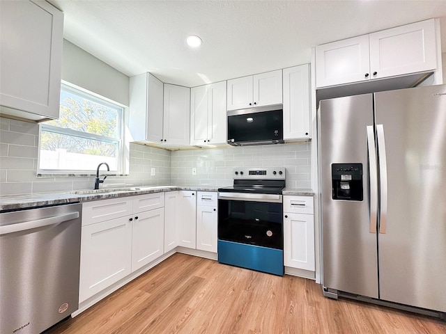 kitchen with stainless steel appliances, light wood finished floors, a sink, and white cabinetry