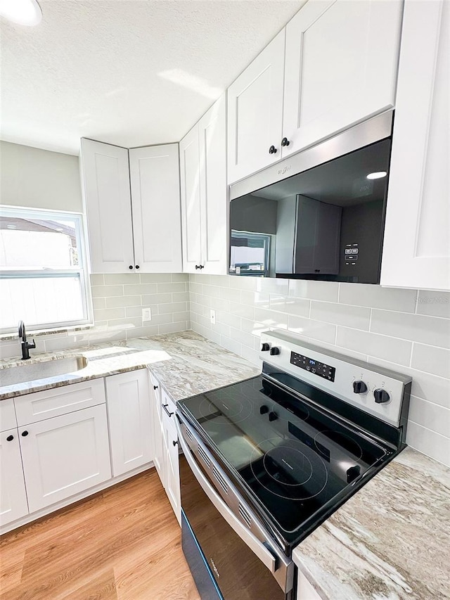 kitchen with stainless steel appliances, a sink, white cabinetry, light wood-style floors, and backsplash