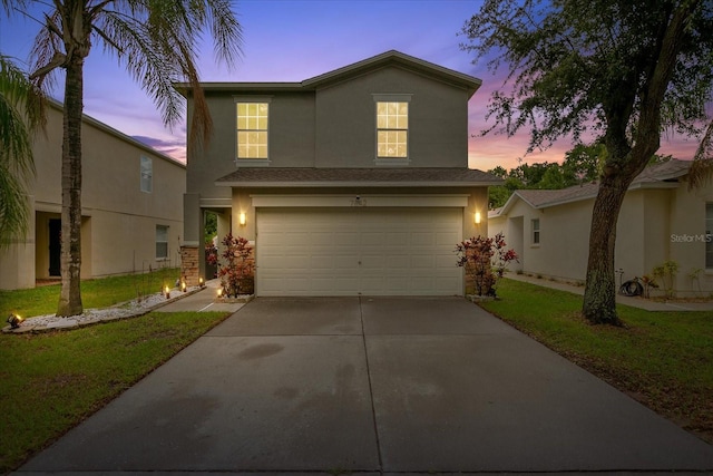 traditional-style house with driveway, an attached garage, a front yard, and stucco siding