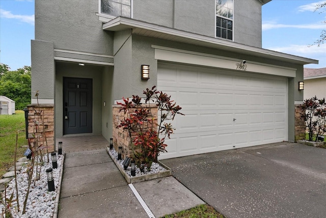 view of exterior entry with driveway, an attached garage, and stucco siding