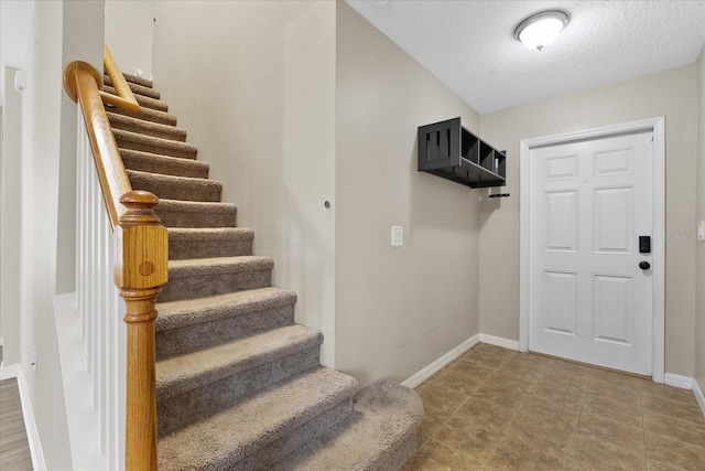 entryway featuring stairway, a textured ceiling, and baseboards