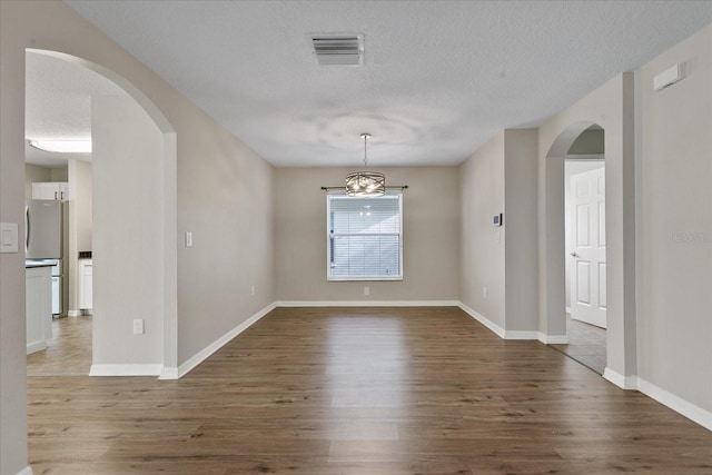 spare room with baseboards, a textured ceiling, arched walkways, and wood finished floors