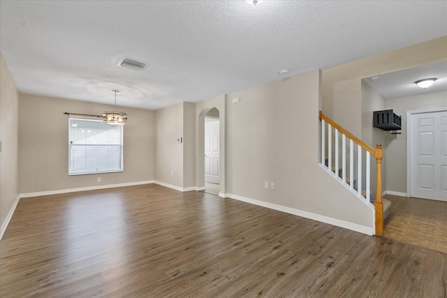 spare room featuring arched walkways, visible vents, stairway, wood finished floors, and baseboards