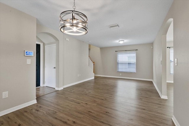 empty room featuring arched walkways, baseboards, stairway, wood finished floors, and a notable chandelier