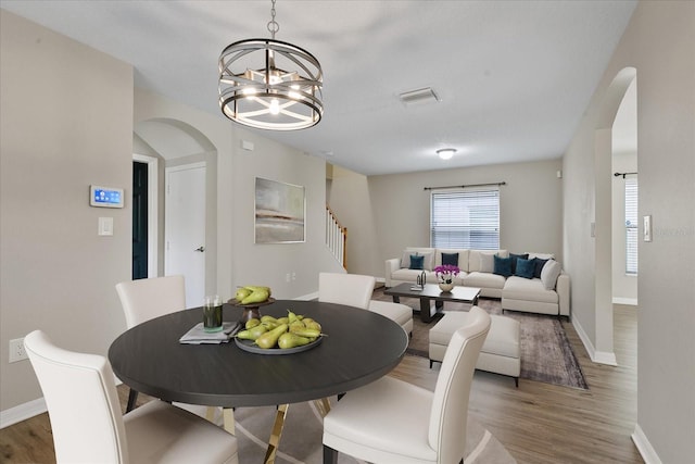 dining area with arched walkways, a notable chandelier, baseboards, and wood finished floors