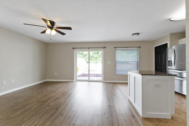 interior space with a textured ceiling, white cabinetry, stainless steel fridge with ice dispenser, light wood-type flooring, and a center island