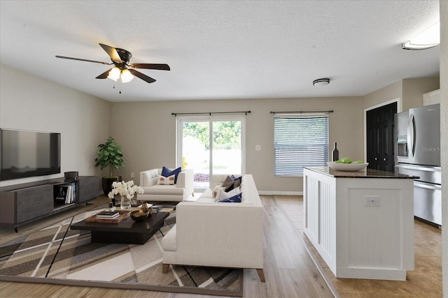 living room featuring ceiling fan, a textured ceiling, and light wood finished floors