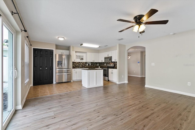 kitchen featuring arched walkways, open floor plan, appliances with stainless steel finishes, decorative backsplash, and dark countertops