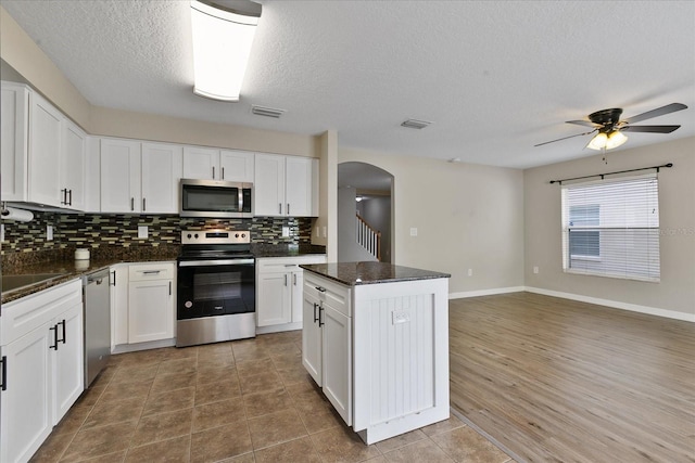 kitchen with visible vents, arched walkways, a kitchen island, stainless steel appliances, and backsplash