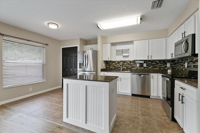 kitchen with stainless steel appliances, tasteful backsplash, white cabinets, a sink, and a kitchen island