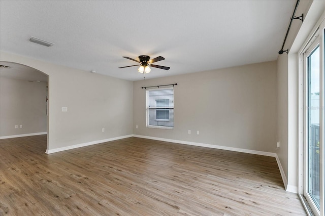 empty room featuring light wood-type flooring, visible vents, arched walkways, and a ceiling fan