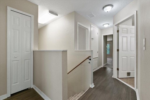 hall with a textured ceiling, visible vents, an upstairs landing, baseboards, and dark wood finished floors