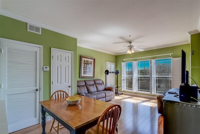 dining room featuring light wood finished floors, a ceiling fan, visible vents, and crown molding