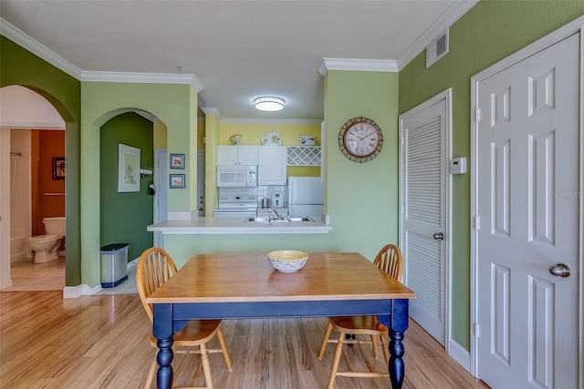 dining area featuring baseboards, visible vents, arched walkways, light wood-style flooring, and crown molding