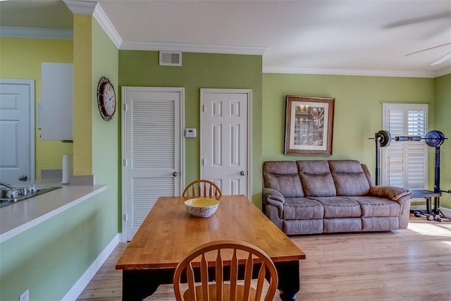 dining space featuring baseboards, light wood finished floors, visible vents, and crown molding