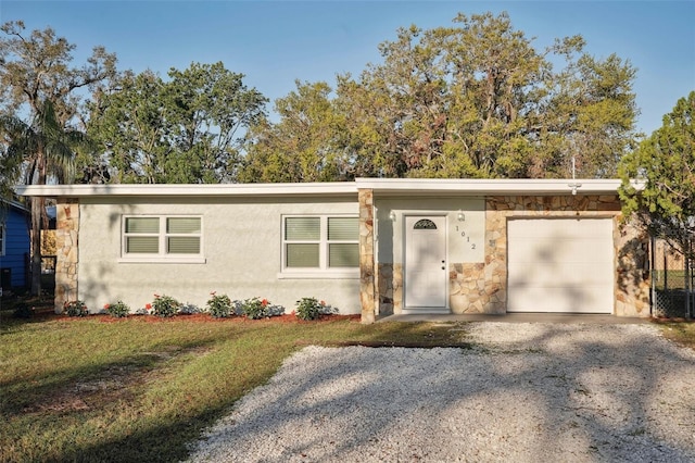 view of front of home featuring stone siding, an attached garage, gravel driveway, a front lawn, and stucco siding