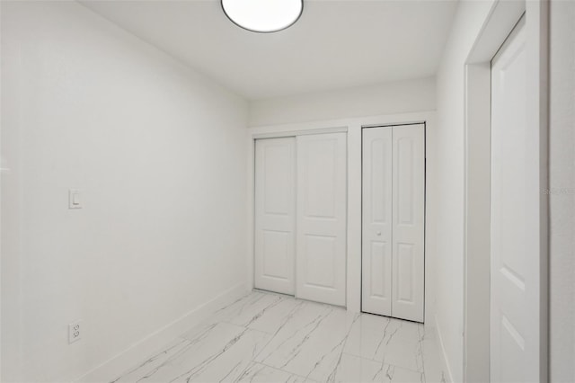 unfurnished bedroom with marble finish floor, two closets, and baseboards